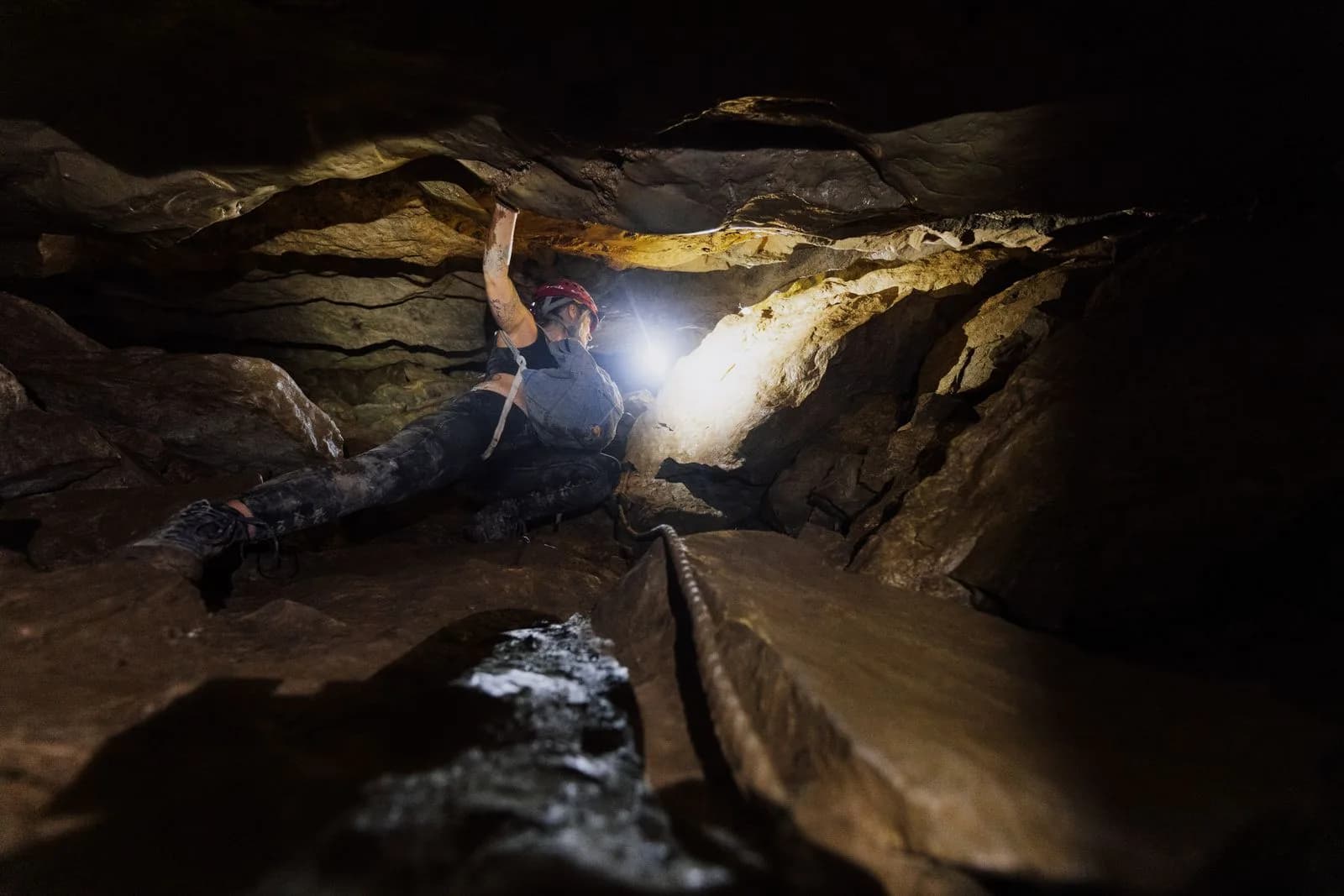 Caver in a helmet and headlamp squeezing through a rocky cave passage